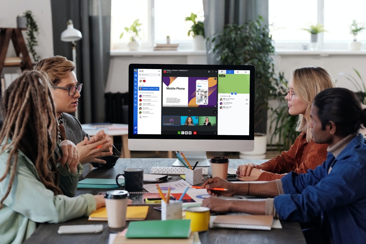 Use Rainbow Hybrid during a meeting Group of professionals having a meeting and looking towards a desktop showing Rainbow on the screen